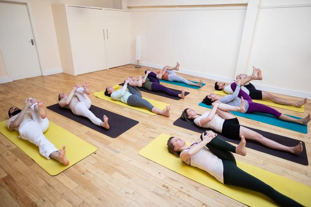 Group of people engaged in stretching exercises during a yoga class in a bright fitness studio. Ideal for promoting fitness programs, yoga classes, wellness retreats, and healthy lifestyle activities.