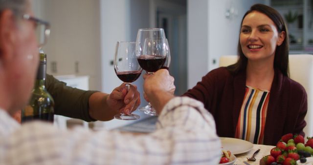 Smiling caucasian mother making a toast with husband and father at table before family meal. multi-generation family enjoying time together at home.