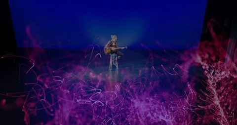 Musician playing acoustic guitar on stage with ambient lighting