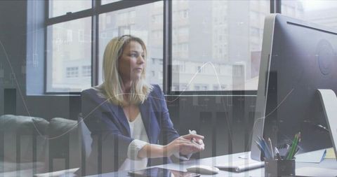 Executive woman analyzing financial charts at desk in modern office with large monitor