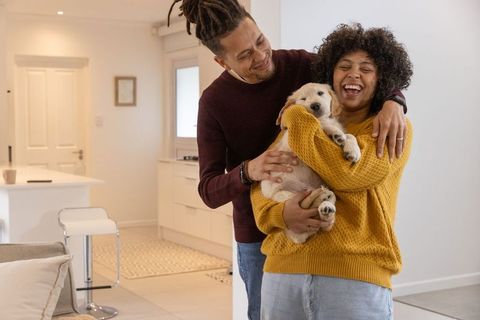 Couple laughing and cradling puppy in modern minimalist kitchen, joyful embrace