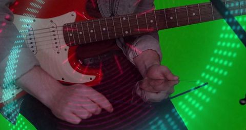 Guitarist playing red electric guitar, sliding with glass slide under neon led lights on green scree