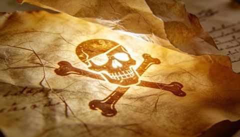 Aged pirate skull crossbones on weathered vellum closeup, handwritten script, warm lamp glow