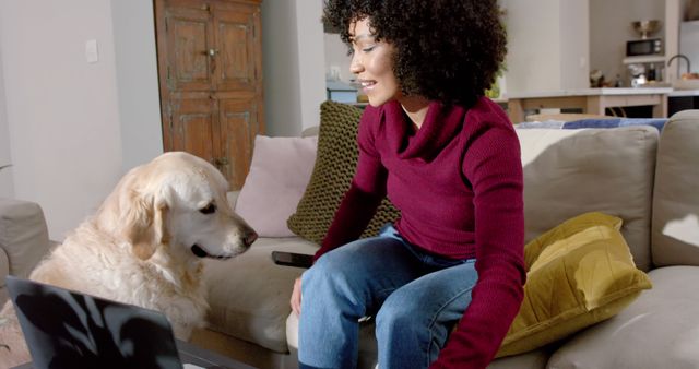 Happy biracial woman with golden retriever dog using laptop at home. Lifestyle, animal, communication and domestic life, unaltered.