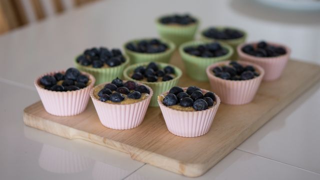Freshly baked blueberry muffins sitting in pastel-colored silicone cups arranged on wooden board. Ideal for use on food blogs, recipe sites, baking tutorials, and in kitchen-themed promotional materials.