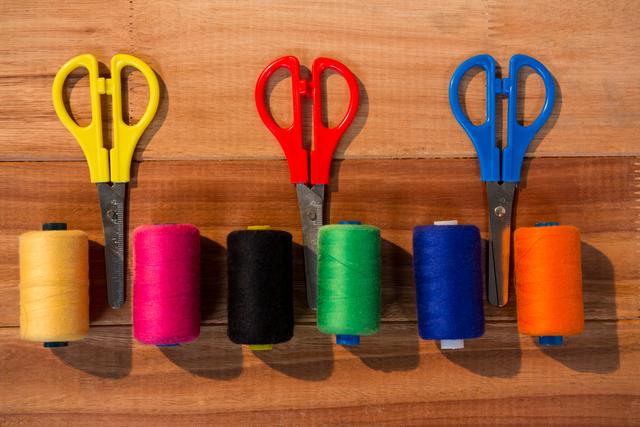 Colorful thread spools and scissors arranged neatly on a wooden table. Ideal for use in articles or advertisements related to sewing, crafting, DIY projects, and textile arts. Perfect for illustrating concepts of creativity, handmade crafts, and tailoring.