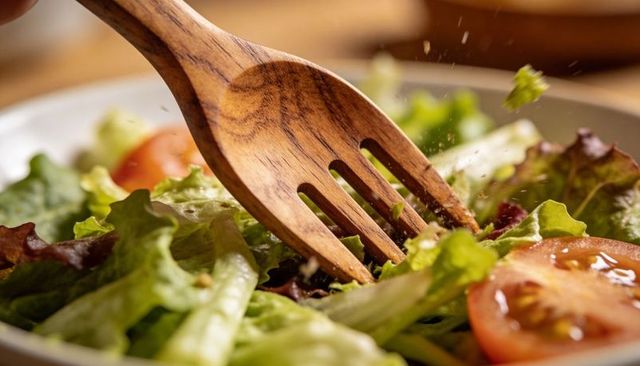 Wooden fork tossing fresh garden salad with tomatoes and olive oil dressing closeup