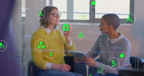 Businesswomen Discussing Sustainable Finance with Floating Eco Icons on Tablet