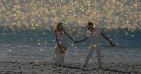 Romantic couple walking hand in hand on sunlit beach wearing white outfits and straw hats