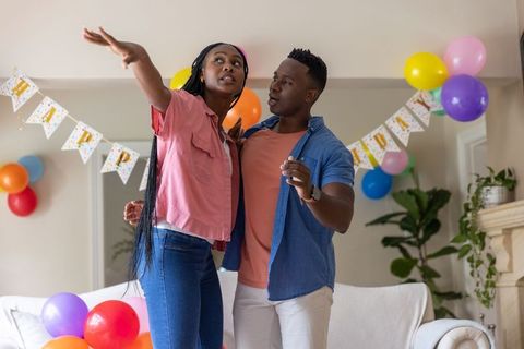African american couple decorating living room with balloons and happy banner for celebration