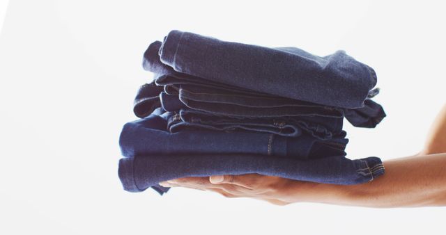 Hands holding folded jeans with different shades on white background with copy space, slow motion. Denim day, material, style and design concept.