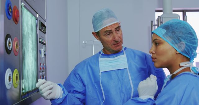 Two medical professionals in blue surgical gowns are reviewing patient X-rays on a screen in a hospital setting. They are discussing the diagnosis and treatment, emphasizing teamwork and medical consultation. This can be used in medical, healthcare, and educational materials to illustrate scenes of professional healthcare environments.