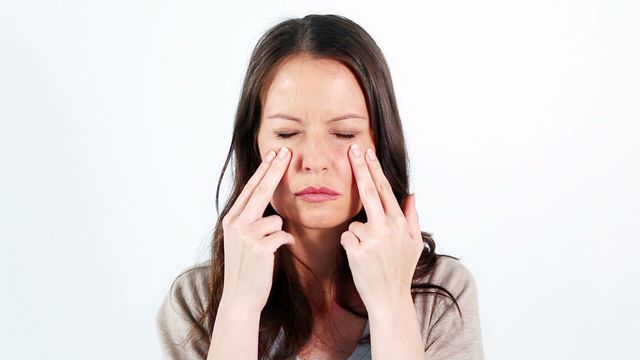 Woman standing against neutral background practicing facial massage. Ideal for content on facial wellness practices, skincare routines, or promoting health and relaxation. Useful in advertisements for skincare products or blogs discussing beauty techniques.