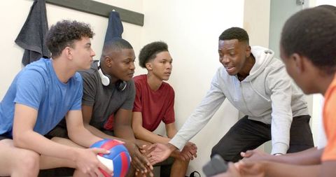 Volleyball team receiving leadership talk from african american coach in locker room huddle