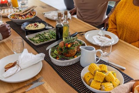 Friends enjoying roast chicken dinner on wooden table with corn, green beans, gravy