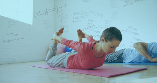 Image shows woman practicing yoga in fitness studio with mathematical equations illustrated in background. She is stretching on pink yoga mat, emphasizing concentration and mindfulness. The setting merges physical fitness with mental exercise, suggesting harmony between body and mind. Perfect for themes on health and wellness, holistic development, mindfulness training, education, and promoting balanced lifestyle.