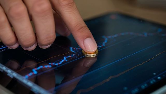 Finger Pressing Gold Coin on Touchscreen Showing Stock Market Candlestick Chart