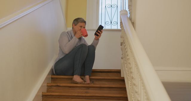 Mature Woman Sitting on Staircase with Coffee and Smartphone in Hand - Download Free Stock Images Pikwizard.com