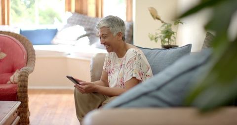 Senior Woman with Grey Hair Smiling While Using Smartphone at Home