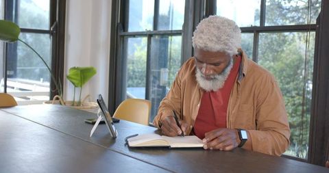 Senior man writing notes at home office with tablet for inspiration and productivity