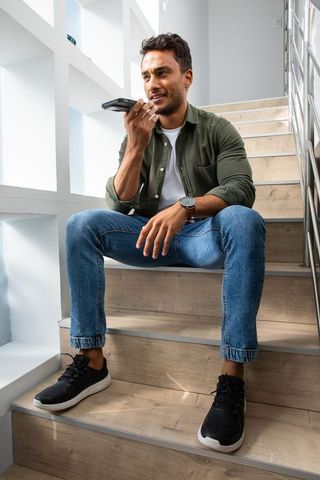 Casually dressed man sitting in stairwell using smartphone voice commands
