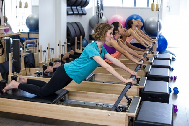 Women performing Pilates exercises on reformers in a well-equipped studio setting. Image suitable for articles and promotions related to fitness, wellness, group fitness classes, exercise equipment, and healthy lifestyles.