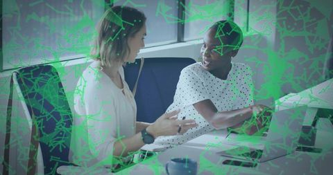 Female colleagues collaborating over laptop with green network overlay in office teamwork
