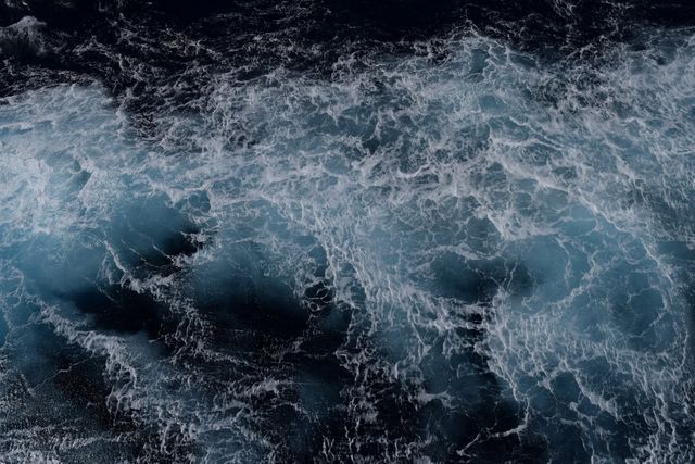 This image captures an aerial view of powerful ocean waves crashing and creating foam. The blue hues and dynamic motion convey the raw energy and beauty of the ocean, making it suitable for travel blogs, environmental websites, presentations about marine life, and backgrounds for designs related to nature or water themes.