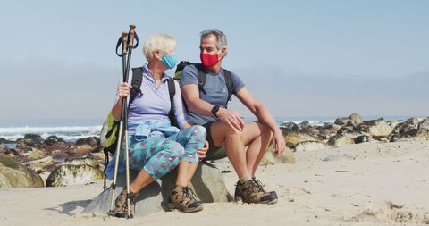 Senior couple in face masks enjoying beach hike