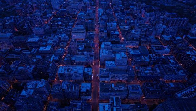 Urban neon city grid at night showing glowing north-south avenue and rooftop hvac patterns