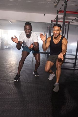 Two male athletes squatting and clapping in gym workout