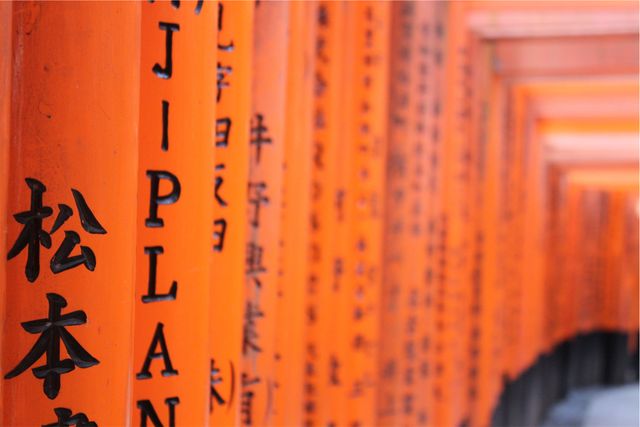 Detailed close-up of traditional Torii gate columns at Fushimi Inari Shrine in Kyoto shows intricate Japanese calligraphy on bright orange wood. Useful for topics on Japanese culture, spirituality, architecture, traditions, or travel promotions. Ideal for cultural articles, travel blogs, educational material, or posters showcasing Japanese heritage.