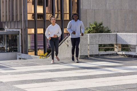 Young couple running together on urban terrace wearing hoodies and joggers in sunlight