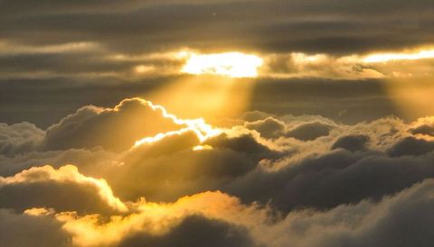 Golden sunbeams piercing layered cumulus clouds at high altitude dawn atmosphere