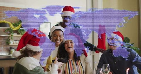 Friends celebrating holiday dinner wearing santa hats viewing phone with world map overlay