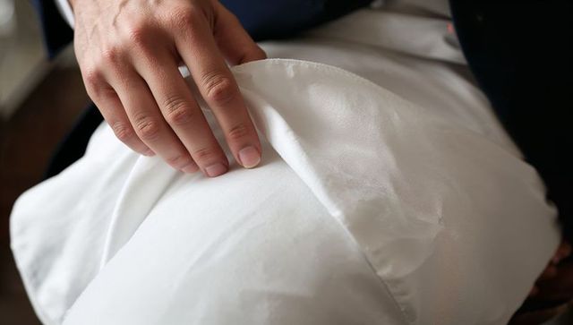 Male hand lifting white satin fabric on lap closeup, dark jacket sleeve textile detail