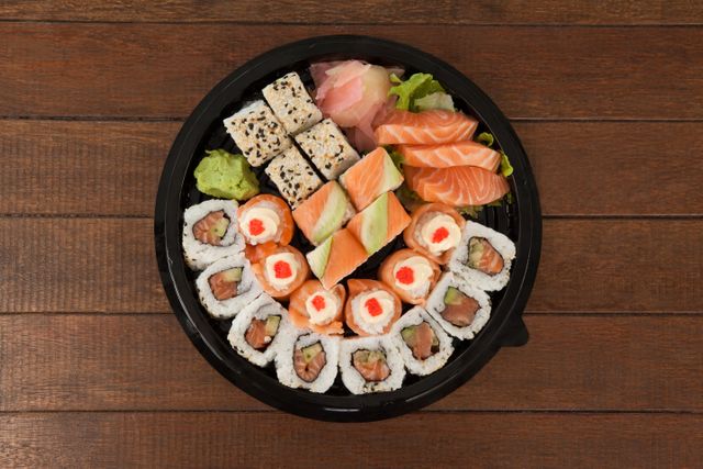 Set of assorted sushi kept in a black round box on wooden table