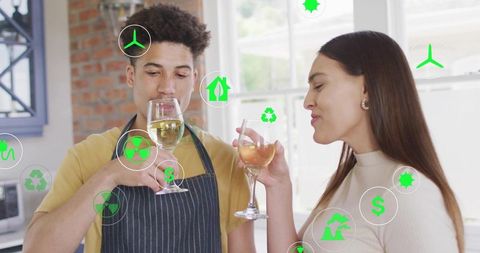 Young couple toasting with wine in modern kitchen surrounded by green sustainability icons
