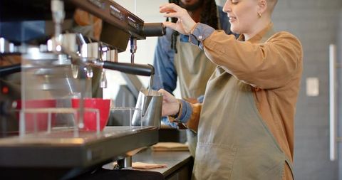Baristas steaming milk with commercial espresso machine behind cafe counter, craft coffee teamwork