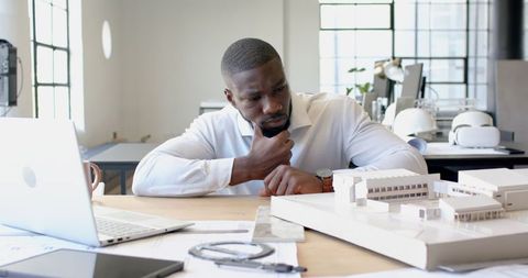 Architect contemplating building model at modern workspace