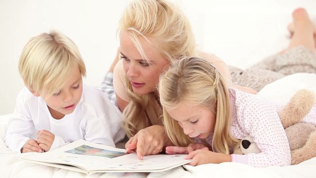 A mother is reading a storybook to her two children while lying in bed. This scene captures a warm, nurturing moment that suggests themes of family, bedtime routines, and early education. It is well-suited for use in articles on parenting, educational blogs, or advertisements focused on home life and family activities.