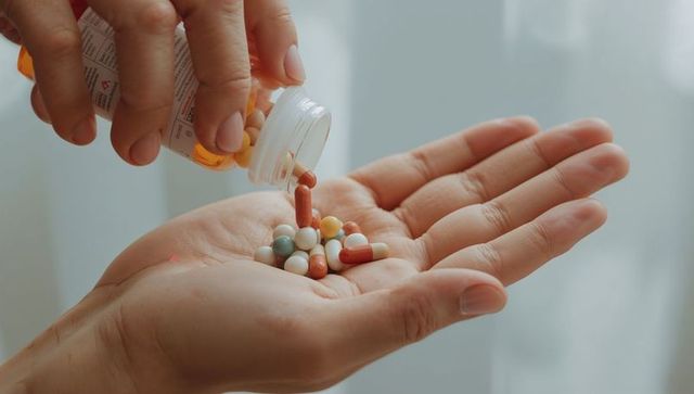 Pouring multicolor capsules into cupped palm from prescription bottle by soft window light