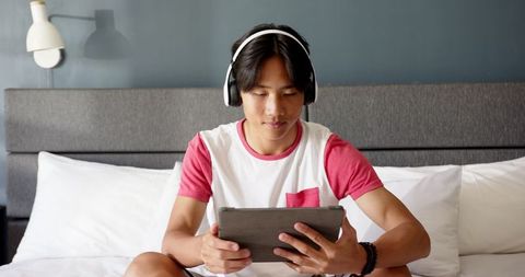 Teen Relaxing in Bedroom Using Tablet and Headphones