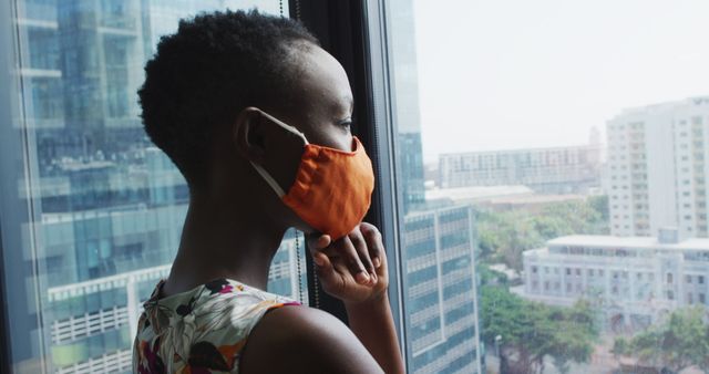 Pensive Young Woman in Face Mask Looking Out Window in Modern Cityscape - Download Free Stock Images Pikwizard.com