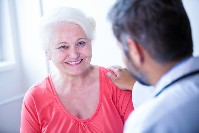 Elderly woman smiles while consulting with a doctor. Useful for depicting healthcare services, patient support, senior care, medical consultations, and doctor-patient relationships in hospital settings. Ideal for use in medical advertisements, healthcare brochures, and informational materials about elderly care.