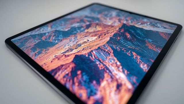 Ultra-thin tablet displaying vibrant mountain wallpaper with metal frame and thin bezels