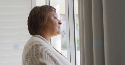 Mature woman gazing through sliding glass door, soaking calm natural light at home