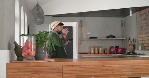 Indian man sipping drink while checking smartphone at modern rustic kitchen island