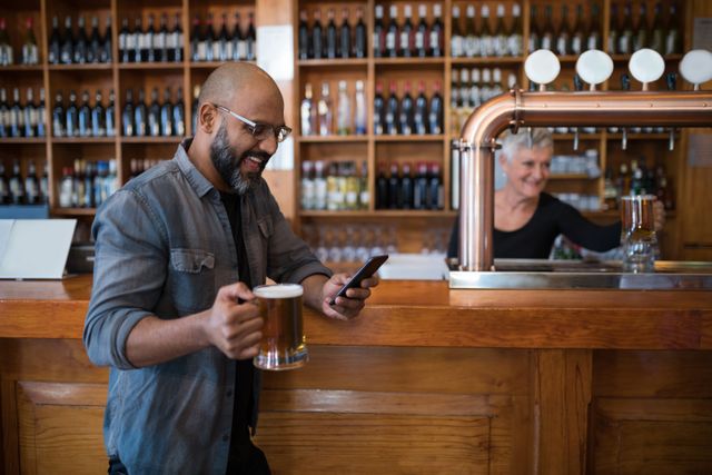 Man enjoying a beer while using his mobile phone in a bar. Ideal for themes related to leisure, socializing, technology, and relaxation. Perfect for advertisements, blog posts, and articles about nightlife, bars, and modern communication.