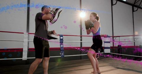 Female boxer training with coach holding focus mitts in boxing ring sparring session - fitness